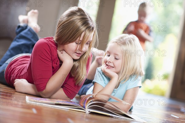 USA, Utah, Girls (6-7, 10-11) reading magazine on floor. Photo : Tim Pannell