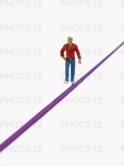 Studio shot of male figurine balancing on tightrope. Photo : David Arky