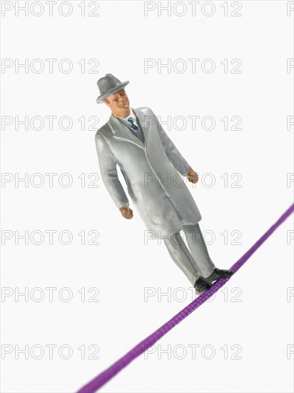 Studio shot of male figurine in suit balancing on tightrope. Photo : David Arky