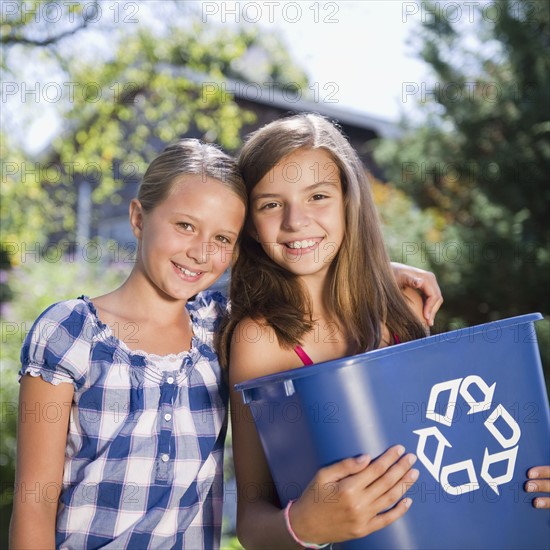 USA, New York, Two girls (10-11, 10-11) holding recycling bin. Photo : Jamie Grill Photography