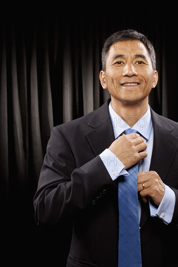 USA, Utah, Provo, Portrait of businessman standing in front of black curtain and adjusting tie. Photo : FBP