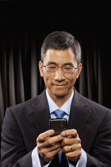 USA, Utah, Provo, Smiling businessman standing in front of black curtain and text messaging. Photo : FBP