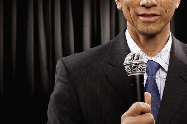 USA, Utah, Provo, Close-up of businessman with microphone standing in front of black curtain, mid section. Photo : FBP