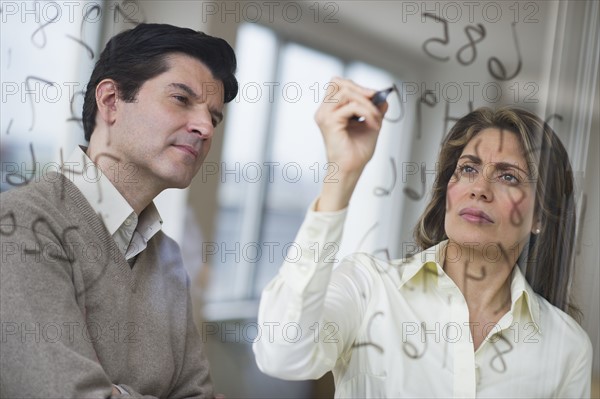 USA, New Jersey, Jersey City, Businessman and woman writing calculations on glass.
