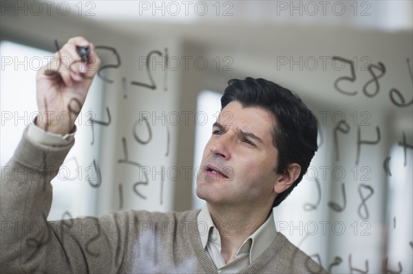 USA, New Jersey, Jersey City, Businessman writing calculations on glass.