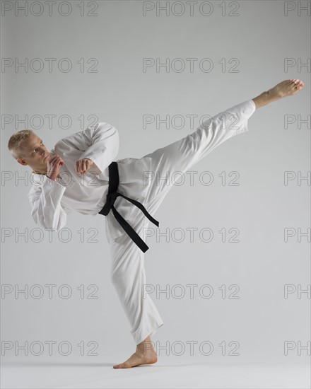 Young man performing karate kick on white background.