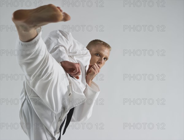 Young man performing karate kick on white background.