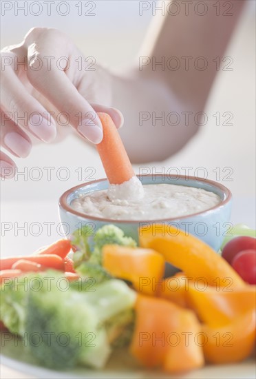 USA, New Jersey, Jersey City, Close-up view of woman hand putting baby carrot into dip. Photo : Jamie Grill Photography