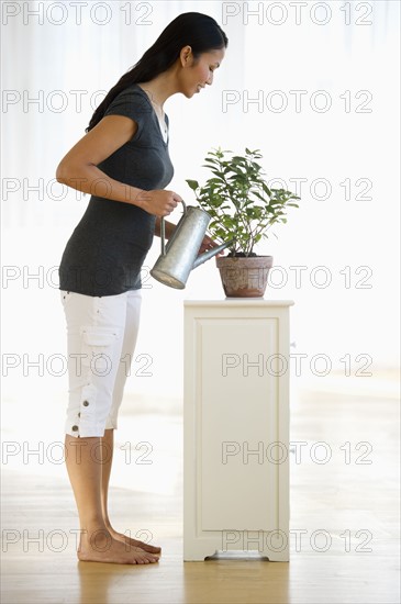 USA, New Jersey, Jersey City, Woman watering plant in home.