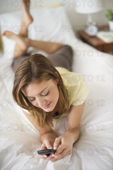 USA, New Jersey, Jersey City, Young woman lying on bed with mobile phone.