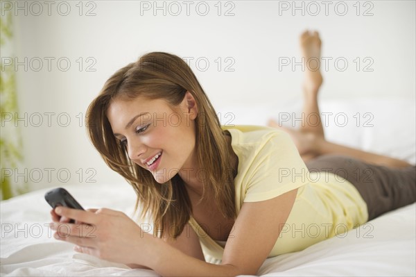 USA, New Jersey, Jersey City, Young woman lying on bed with mobile phone.