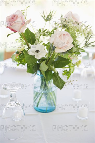 Vase of roses on set dinner table with glasses.