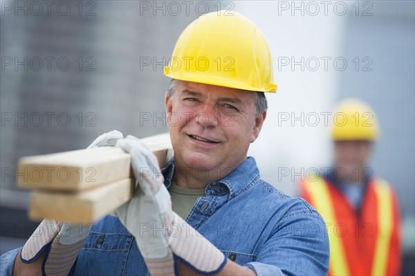 USA, New Jersey, Jersey City, Portrait of construction worker carrying planks.