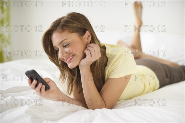 USA, New Jersey, Jersey City, Young woman lying on bed with mobile phone.