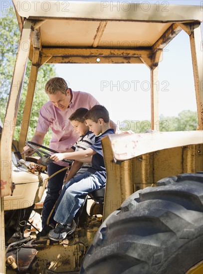 USA, New York, Flanders, Two boys (4-5, 8-9) with father sitting on tractor. Photo : Jamie Grill Photography