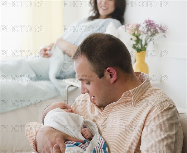 USA, New Jersey, Jersey City, father embracing baby daughter (2-5 months) with mother in background. Photo : Jamie Grill Photography