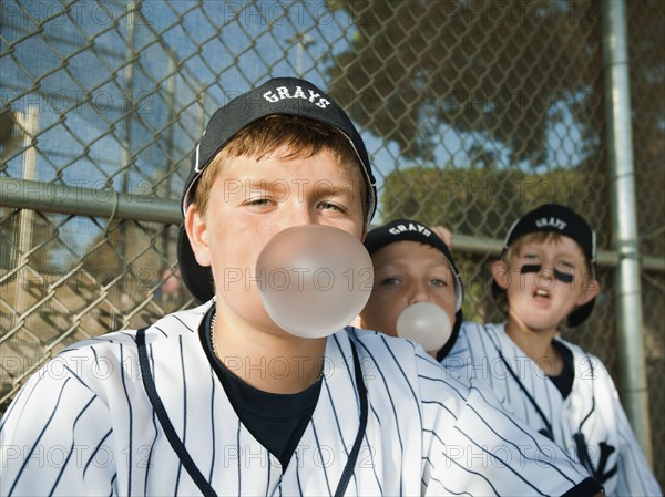 USA, California, Ladera Ranch, Boys (10-11) from little league sitting on dugout and blowing bubble gum.