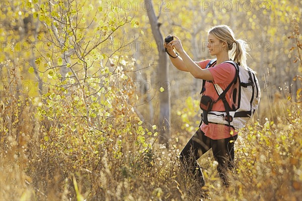 USA, Utah, young woman taking photograph in forest. Photo : Mike Kemp