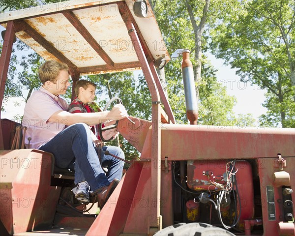 USA, New York, Flanders, Boy (8-9) with father sitting on tractor. Photo : Jamie Grill Photography