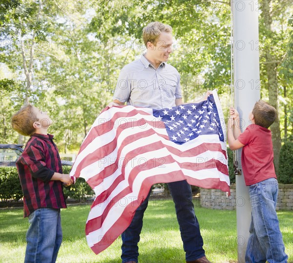 USA, New York, Flanders, Father with two boys (4-5, 8-9) hanging American flag on pole. Photo : Jamie Grill Photography