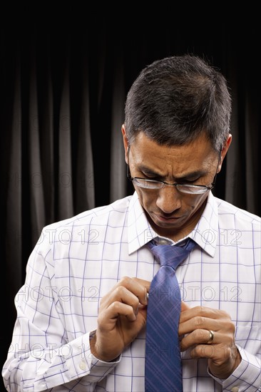 USA, Utah, Provo, Man standing in front of black curtain and adjusting tie. Photo : FBP