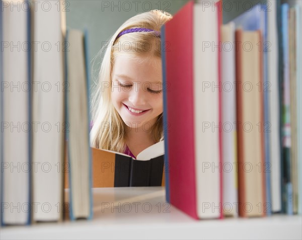 USA, New Jersey, Jersey City, View across the shelf showing girl (8-9) reading book. Photo : Jamie Grill Photography