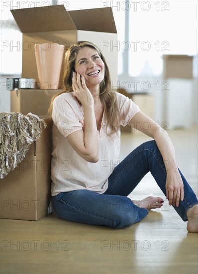 USA, New Jersey, Jersey City, Woman using mobile phone by boxes in new home.