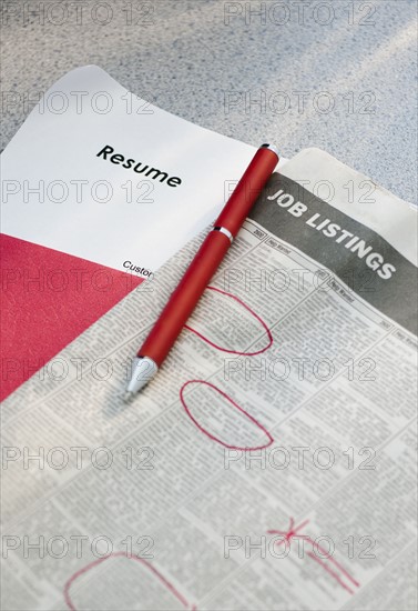 Pen on newspaper job listings with resume.