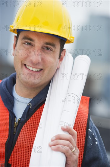 USA, New Jersey, Jersey City, Portrait of construction worker holding blueprints on construction site.