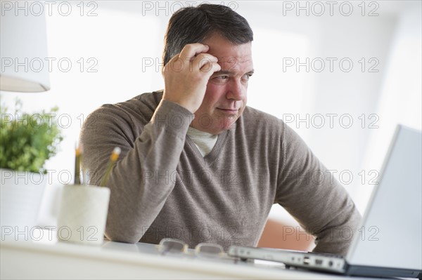 USA, New Jersey, Jersey City, Pensive man using laptop in living room.