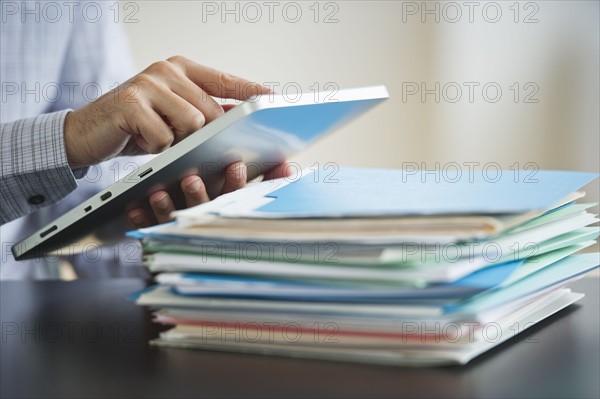 USA, New Jersey, Jersey City, Businessman using digital tablet by paperwork.