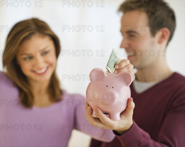 USA, New Jersey, Jersey City, Portrait of young couple putting banknote to piggybank.