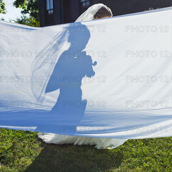 Silhouette of bride behind large sheet in garden.