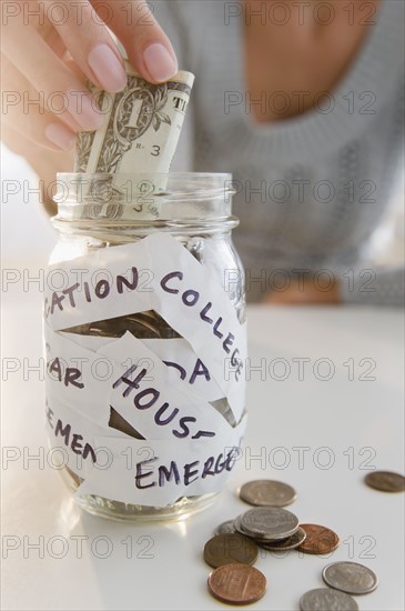USA, New Jersey, Jersey City, Close-up view of woman's hand putting one dollar bill into piggybank. Photo : Jamie Grill Photography