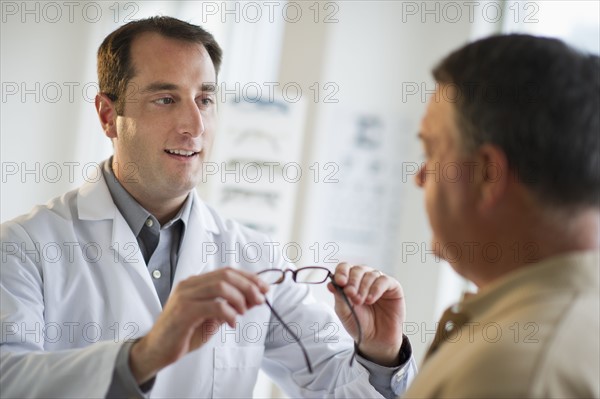 USA, New Jersey, Jersey City, Optician showing man glasses in shop.