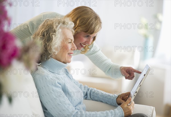 USA, New Jersey, Jersey City, Senior mother and daughter using digital tablet on sofa.