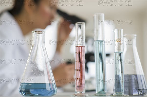 USA, New Jersey, Jersey City, Female scientist using microscope behind test tubes and flasks.