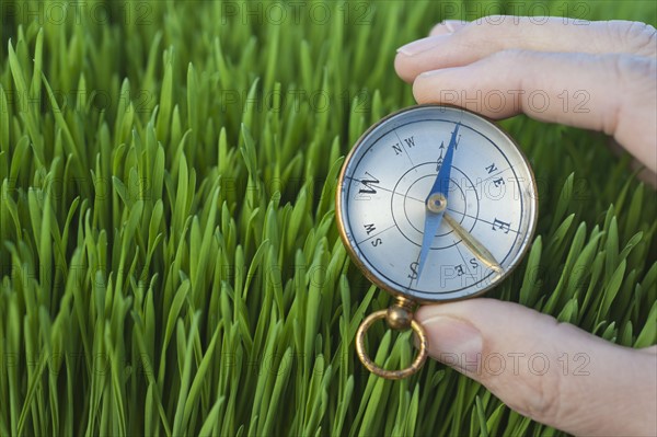 Male hand holding compass over grass.