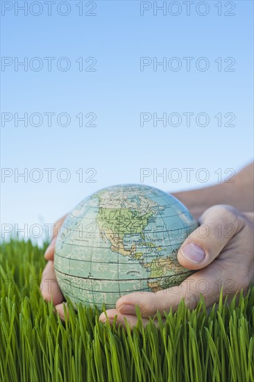 Male hands holding globe over grass.