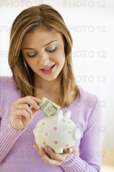 USA, New Jersey, Jersey City, Portrait of young woman putting banknote to piggybank.