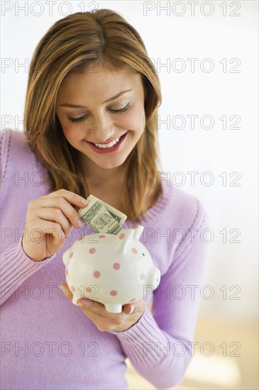 USA, New Jersey, Jersey City, Portrait of young woman putting banknote to piggybank.