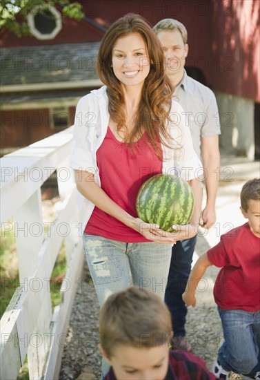 USA, New York, Flanders, Mother holding water melon while boys (4-5, 8-9) are messing about, father in background. Photo : Jamie Grill Photography