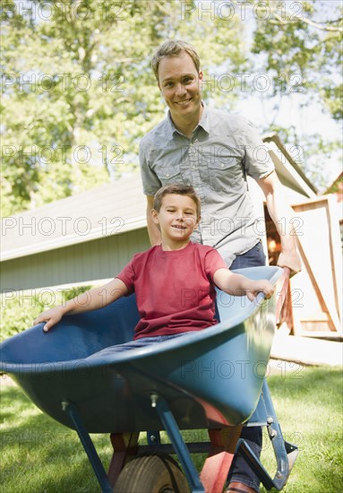 USA, New York, Flanders, father pushing wheel barrow with son (8-9) inside. Photo : Jamie Grill Photography