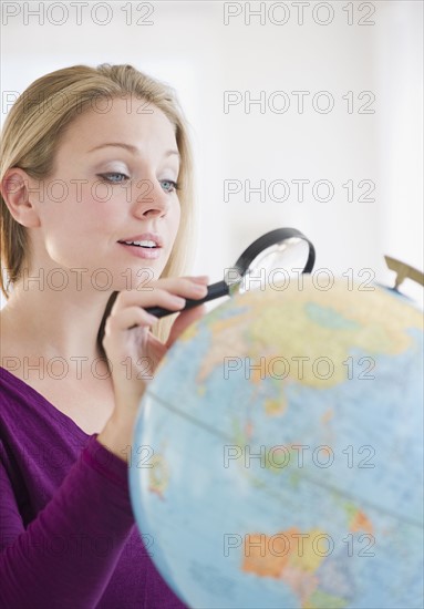 USA, New Jersey, Jersey City, Attractive young woman examining globe with magnifying glass. Photo : Jamie Grill Photography