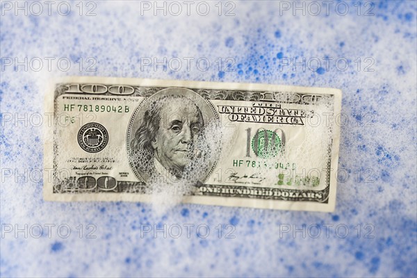 One hundred dollar bill soaking in soap sud. Photo : Mike Kemp