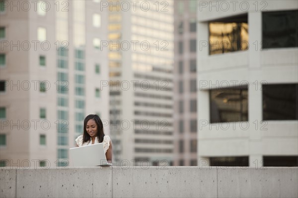USA, Utah, Salt Lake City, Young businesswoman using laptop in front of skyscrapers. Photo : Mike Kemp
