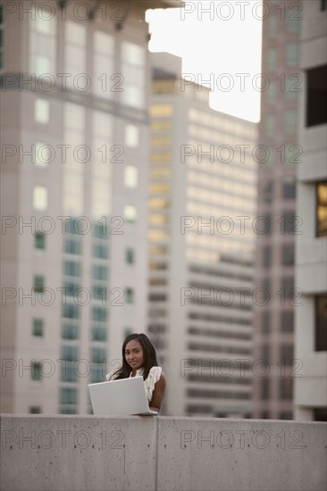 USA, Utah, Salt Lake City, Young businesswoman using laptop in front of skyscrapers. Photo : Mike Kemp