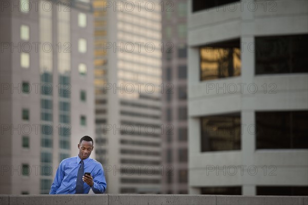 USA, Utah, Salt Lake City, Young businessman text messaging in front of skyscrapers. Photo : Mike Kemp