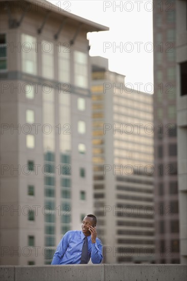 USA, Utah, Salt Lake City, Young businessman talking on mobile phone in front of skyscrapers. Photo : Mike Kemp