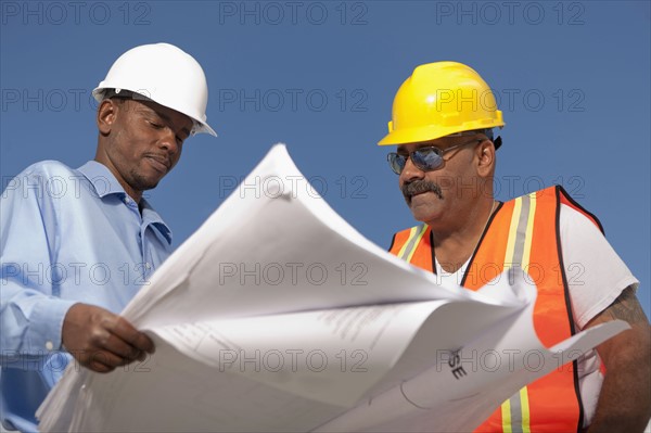 Two construction workers discussing blueprints on building site. Photo : Dan Bannister